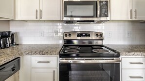 A kitchen with white cabinets, a stainless steel microwave, a stove with four burners, and a coffee maker on the counter.