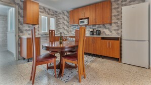 Una cocina con armarios de madera, microondas, refrigerador y una mesa de comedor con sillas.