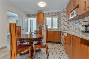 Una cocina con armarios de madera, una mesa de comedor con sillas, un microondas y una cafetera.