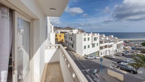 Un balcón con vistas a una calle costera, edificios y el mar.