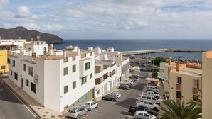 Zona residencial costera con edificios blancos, un puerto deportivo y coches estacionados.