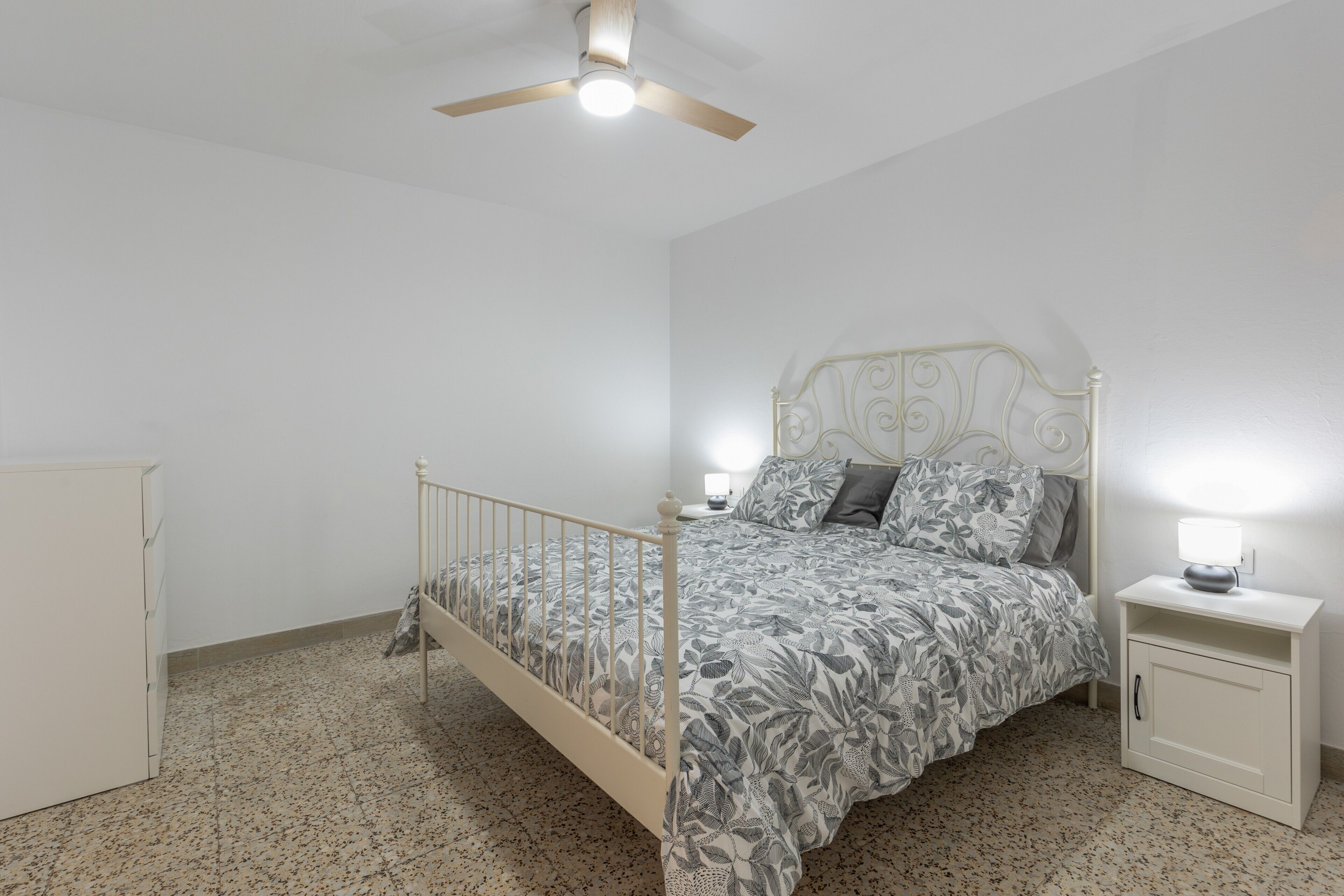 Un dormitorio con cama, mesita de noche, armario y ventilador de techo.