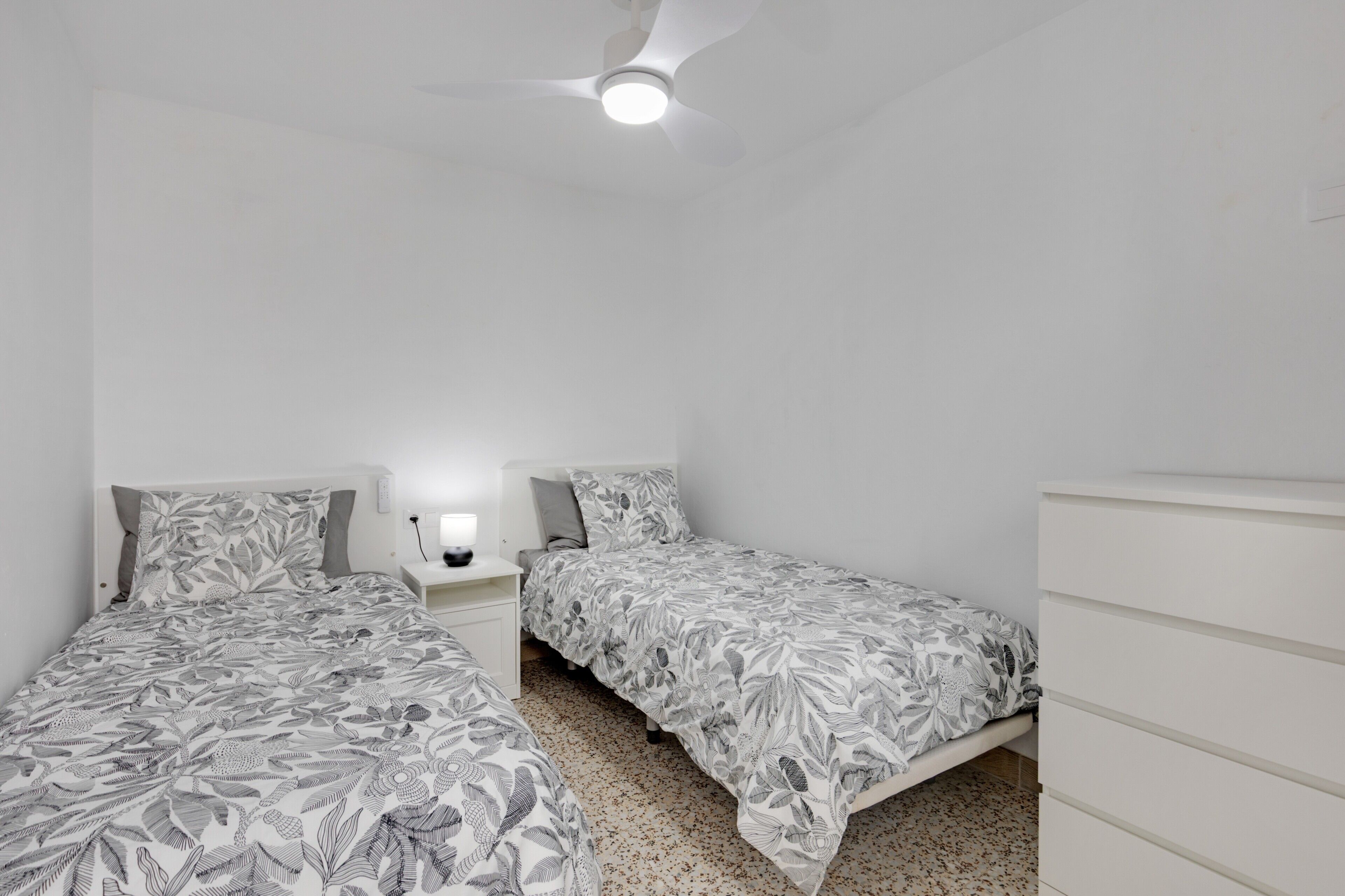 Een slaapkamer met twee bedden, een nachtkastje, een dressoir en een plafondventilator.