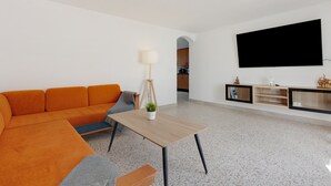 Un salon moderne avec un canapé, une table basse, une lampe et un téléviseur à écran plat fixé au mur.