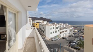 Un balcon donnant sur une rue côtière, des immeubles et une montagne au loin.