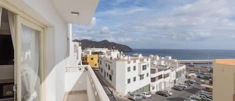 A balcony with a view of a coastal street, buildings, and a mountain in the distance.