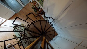 A spiral staircase with a metal railing, wooden steps, and a view of a room with a checkered floor and a plant. - Alojar Towers (Ushuaia)