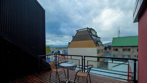 A balcony with a table and chairs, overlooking a cityscape with buildings and mountains. - Alojar Towers (Ushuaia)