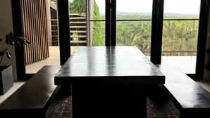 Un interior moderno con una mesa grande y bancos, ventanas amplias que ofrecen vistas a la vegetación y un paisaje lejano.