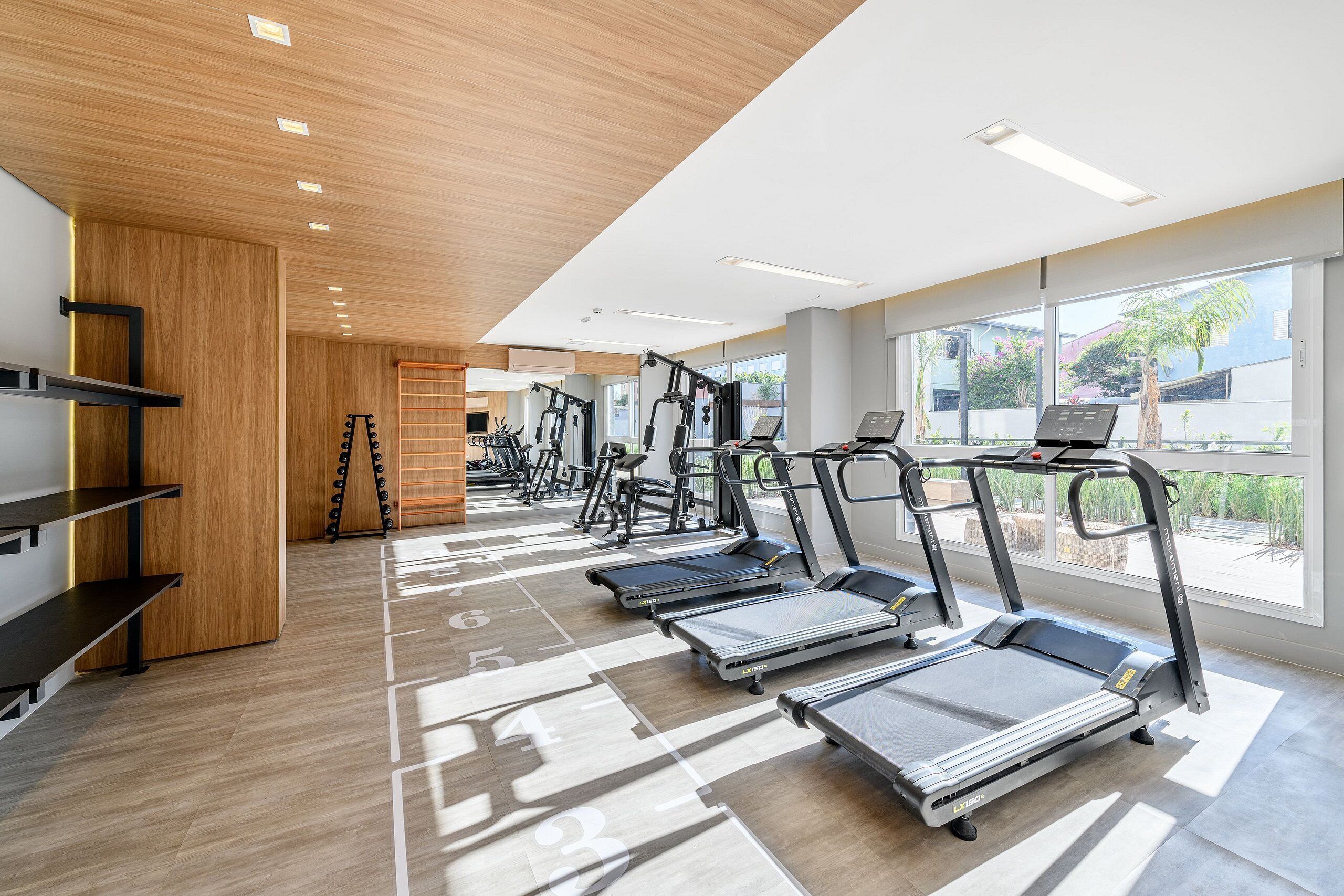 Een fitnessruimte met loopbanden, hometrainers en een houten wand.