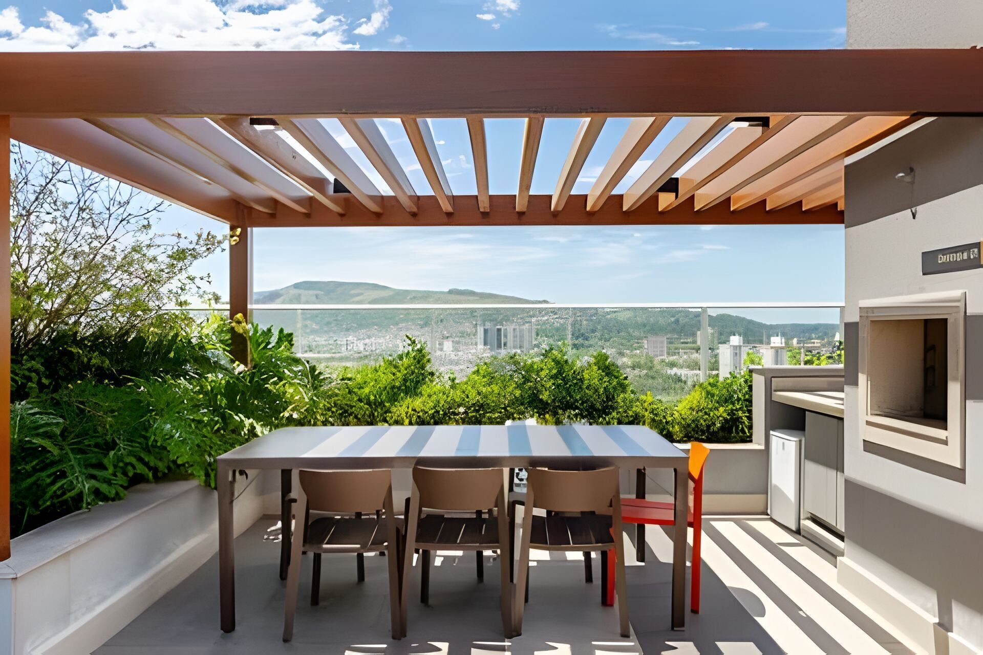 Une terrasse extérieure avec une table et des chaises, une pergola et une vue sur le paysage urbain et les collines.
