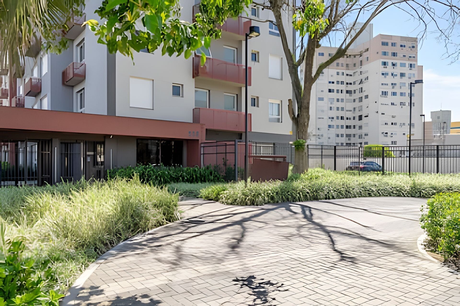 Een modern appartementencomplex met een gebogen oprit, omgeven door groen en een hek.