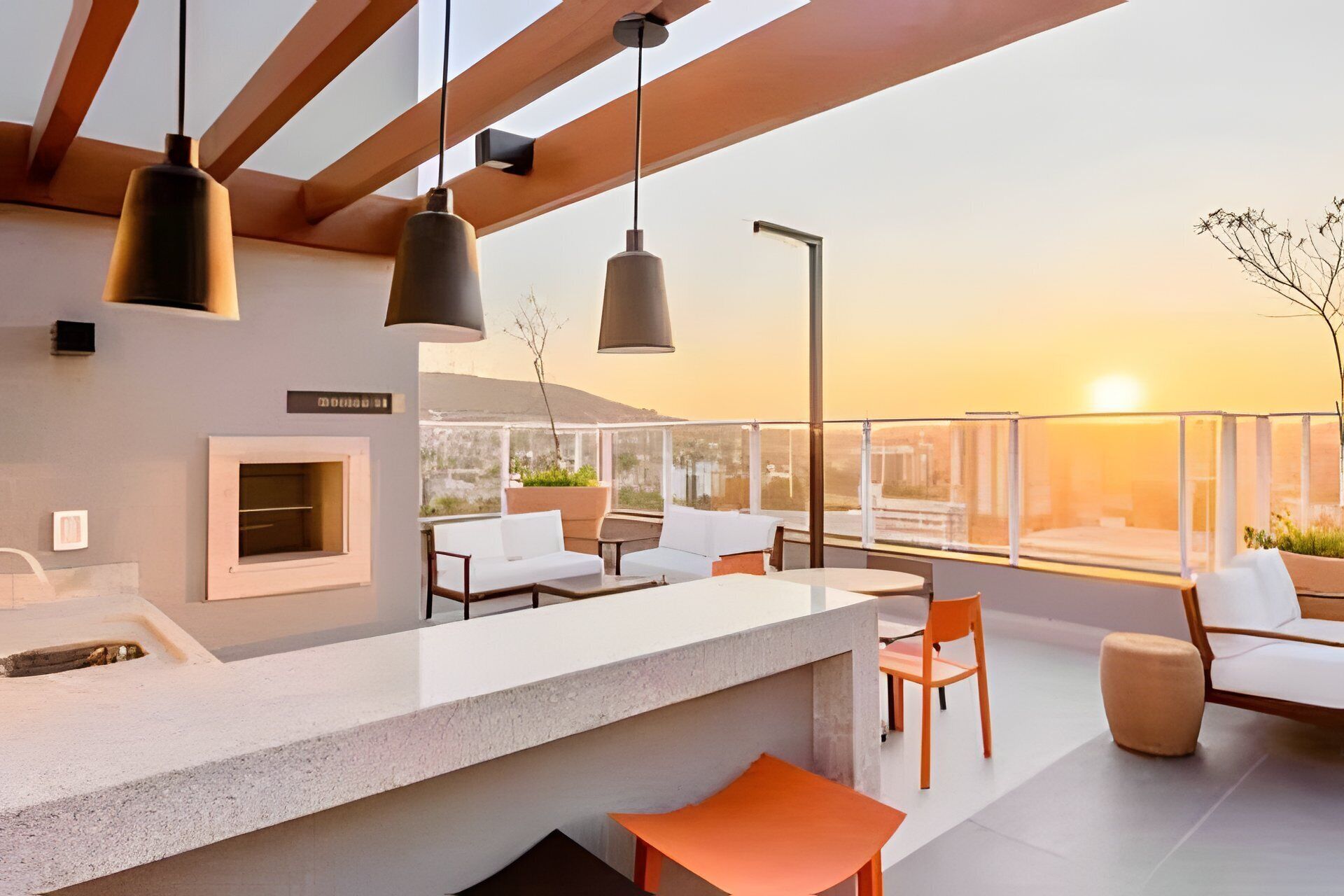 Un espace extérieur moderne aménagé avec des sièges, un bar, des luminaires suspendus et une vue sur le coucher de soleil.