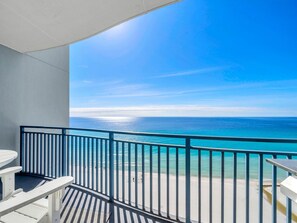 Ein Balkon mit Blick auf den Ozean, weiße Gartenmöbel und ein Metallgeländer.