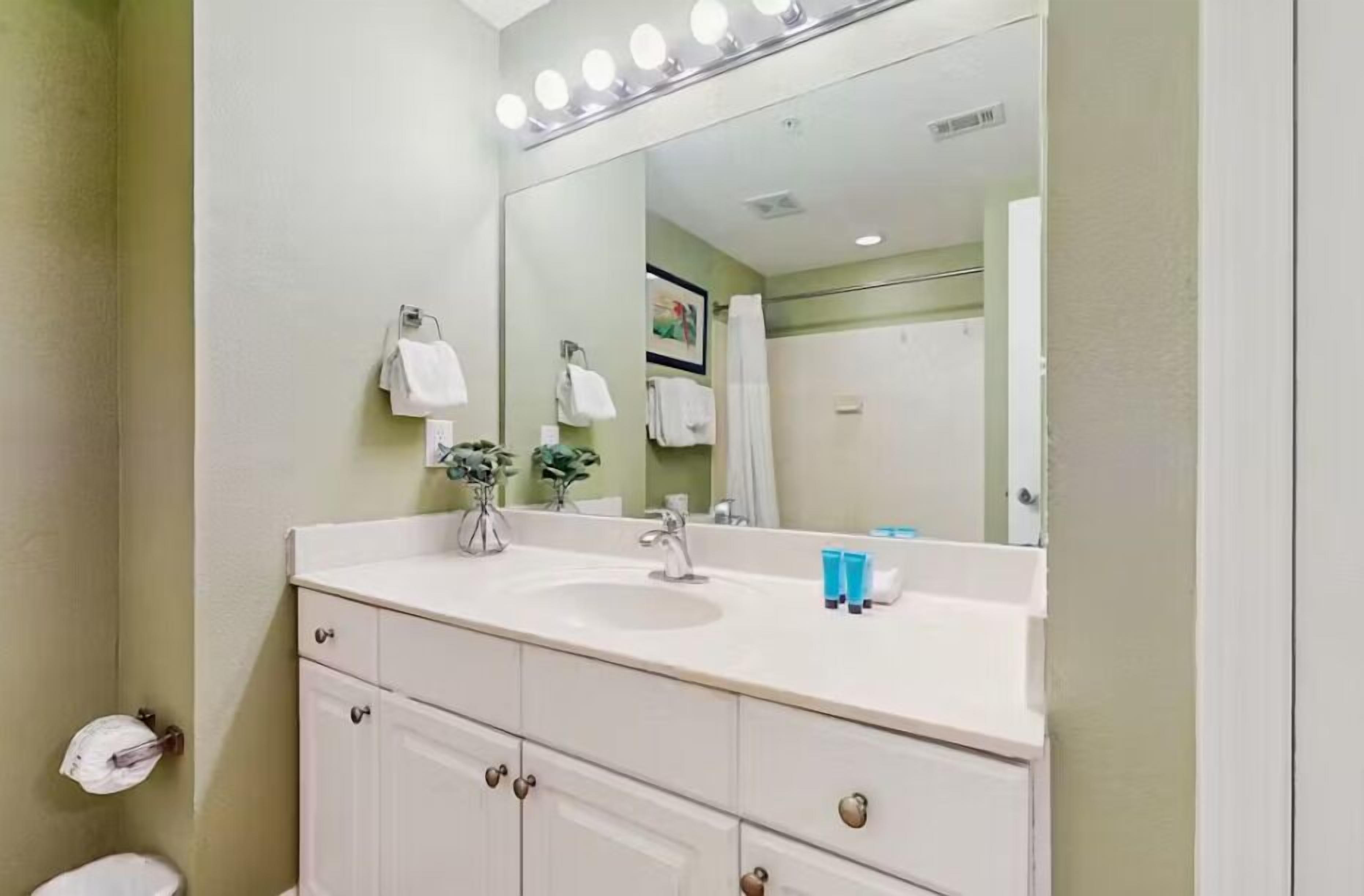 Une salle de bain avec un lavabo blanc, un grand miroir et une commode avec des tiroirs.
