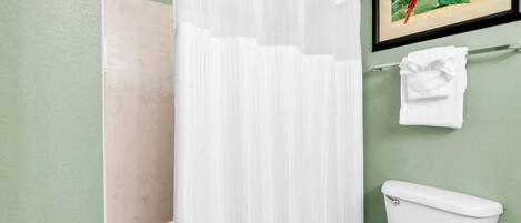 A bathroom with a white bathtub, a white toilet, a white shower curtain, and a framed painting of a parrot on the wall.