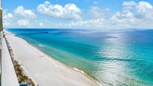 Een strand met een pier die zich uitstrekt over de oceaan, heldere lucht en een wit zandstrand.