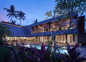 Uma casa moderna com piscina, rodeada por plantas tropicais e palmeiras.