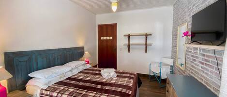 A bedroom with a bed, bedside table, lamp, wardrobe, and a TV mounted on a brick wall.