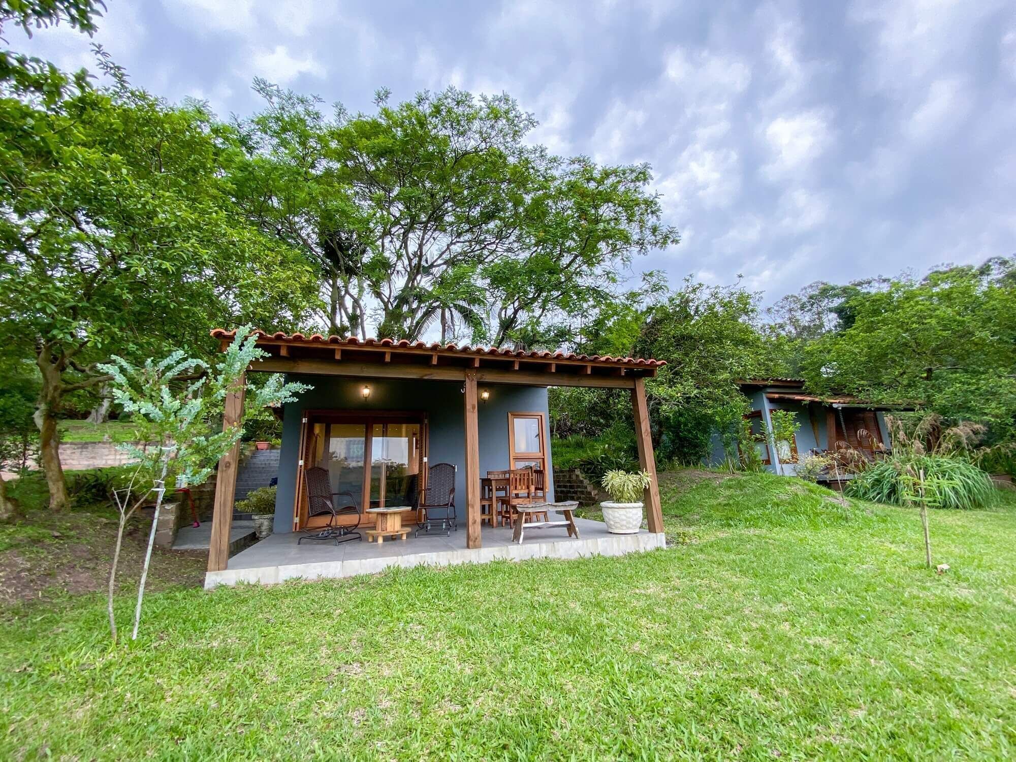 A small, single-story structure with a covered patio area, surrounded by lush greenery and trees.