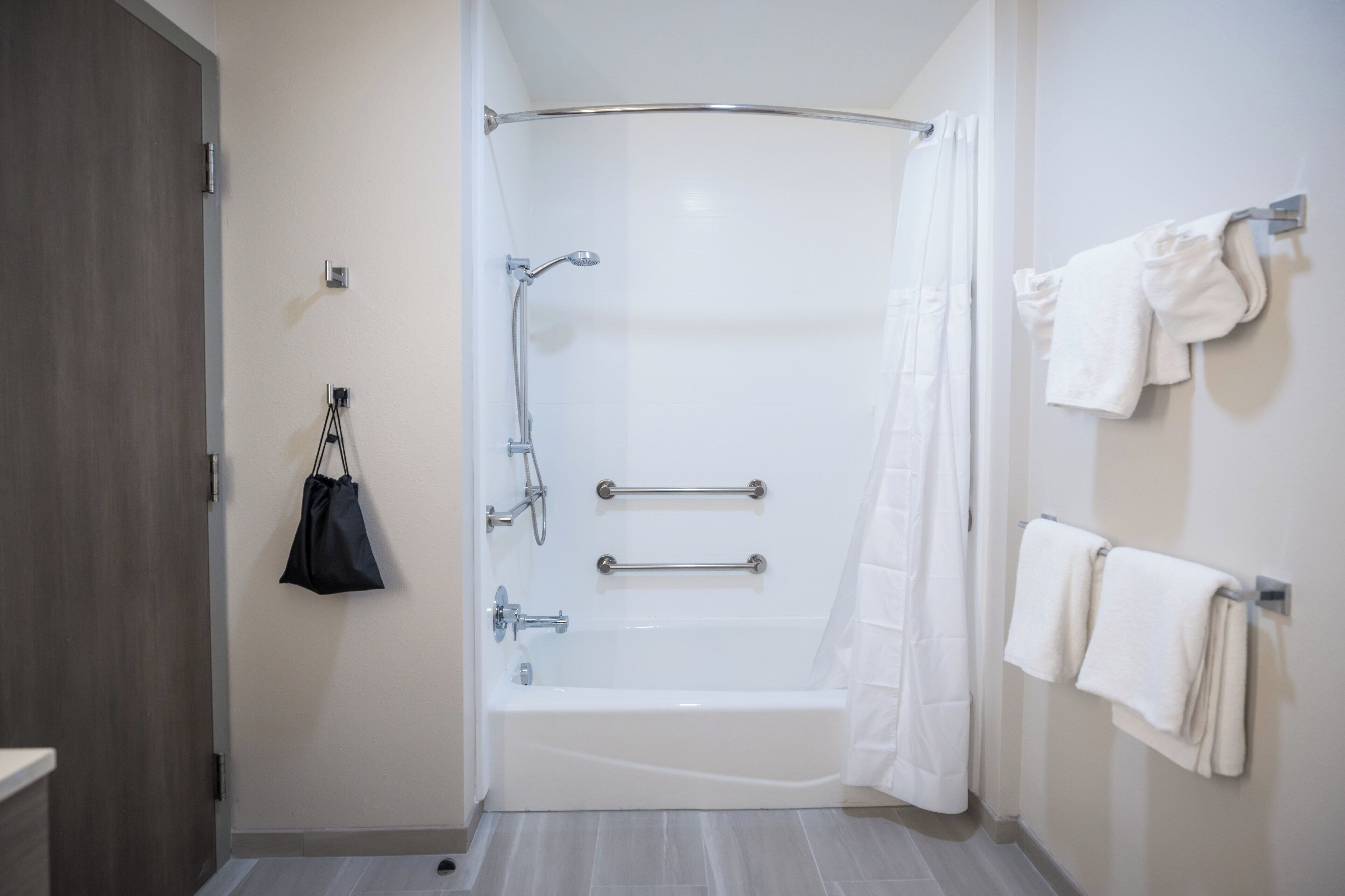 A modern bathroom with a walk-in shower, grab bars, and a towel rack.