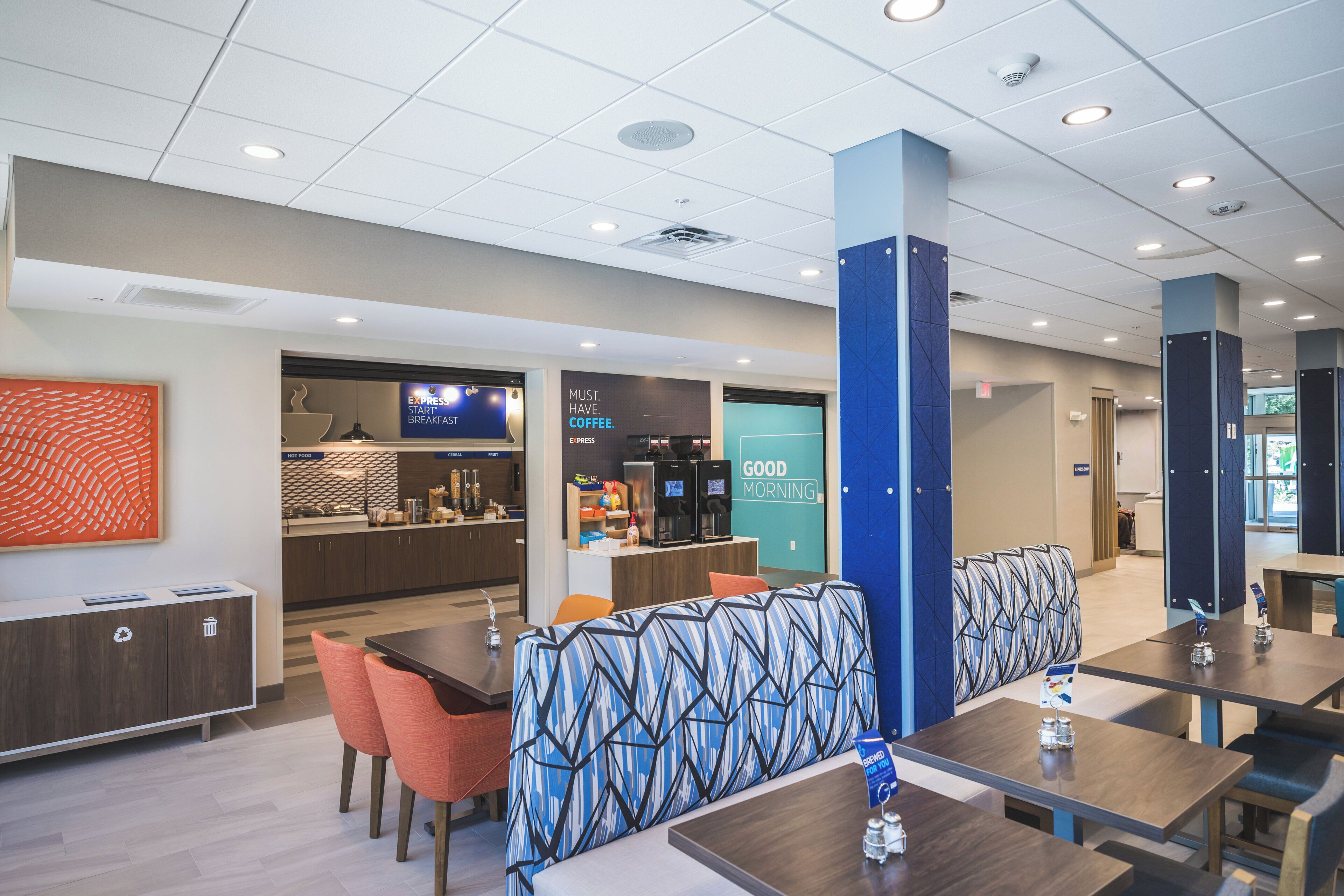 A modern hotel lobby with a coffee station, seating area, and a visible exit sign.