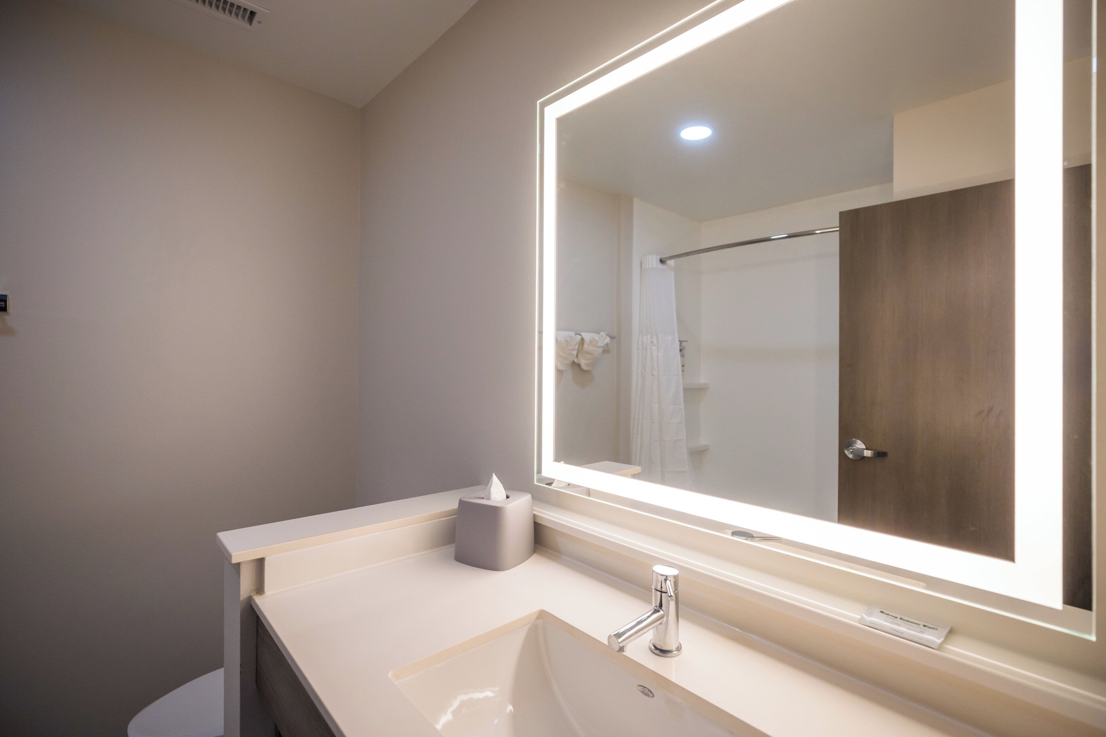 A modern bathroom with a large mirror, a sink, and a shower area.