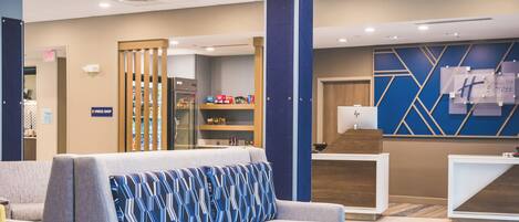 A hotel lobby with a reception desk, seating area, and a kitchenette.