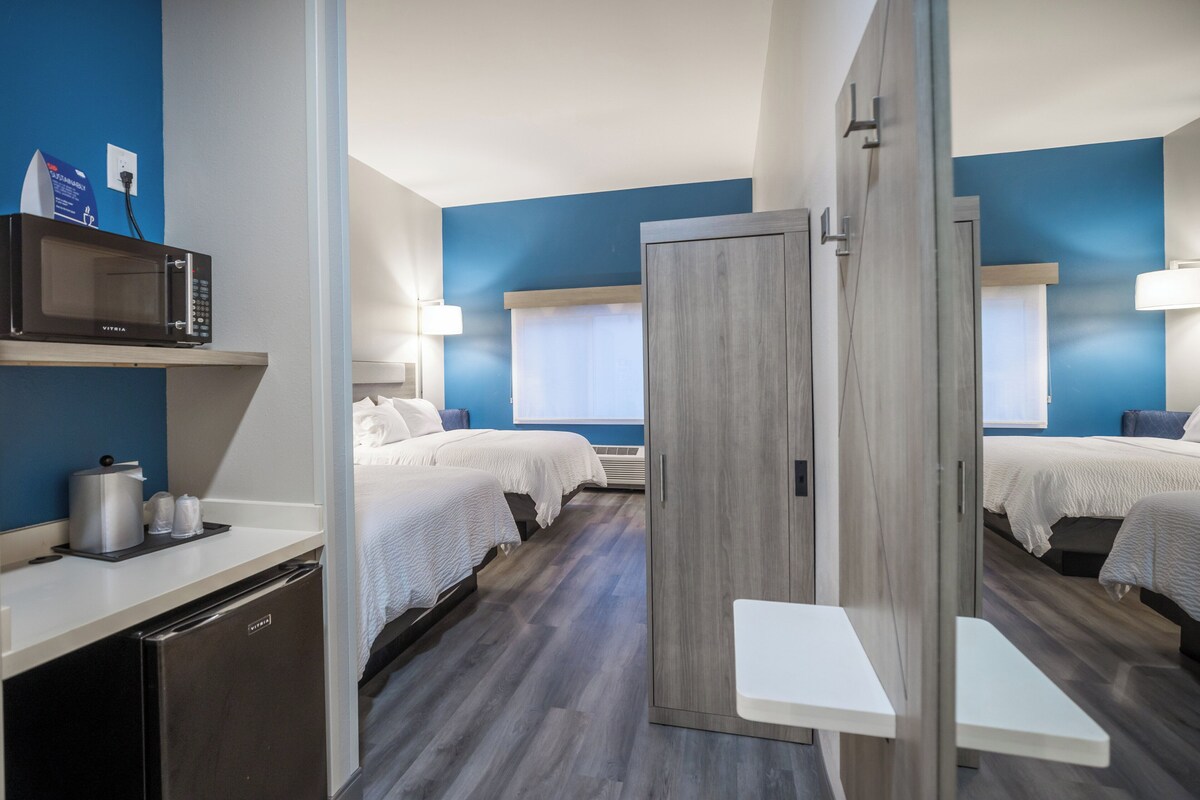Ein Hotelzimmer mit zwei Betten, einer Mikrowelle, einer Kaffeemaschine und einem kleinen Tisch.