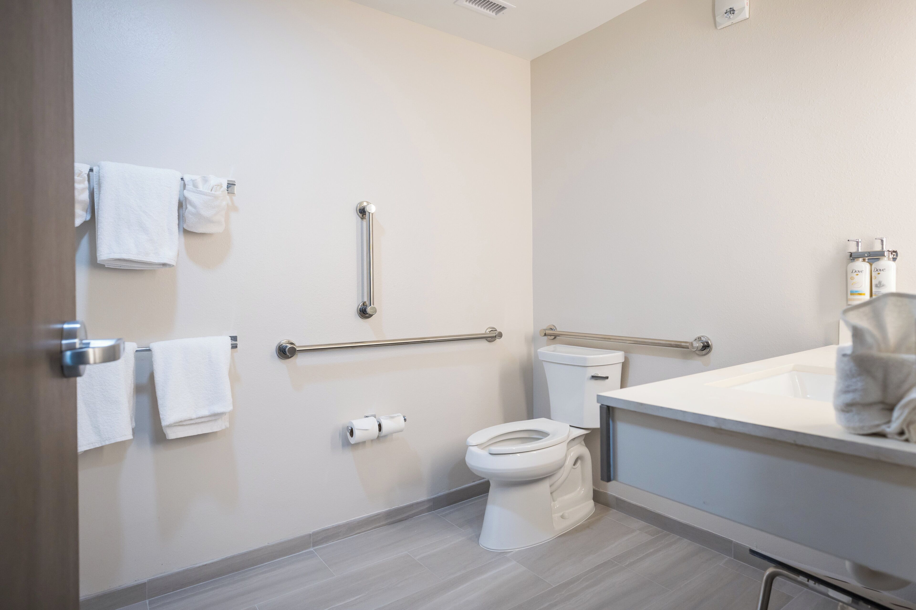 A bathroom with a toilet, handrails, a towel rack, and a sink.