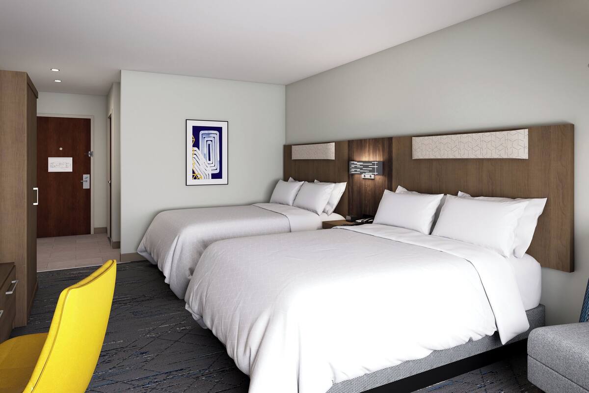 Ein Hotelzimmer mit zwei Betten, einem Holzkopfteil, einem gerahmten Bild an der Wand und einem gelben Stuhl.