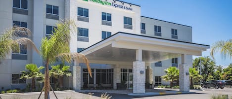 A Holiday Inn Express & Suites building with a covered entrance, palm trees, and a clear sky.