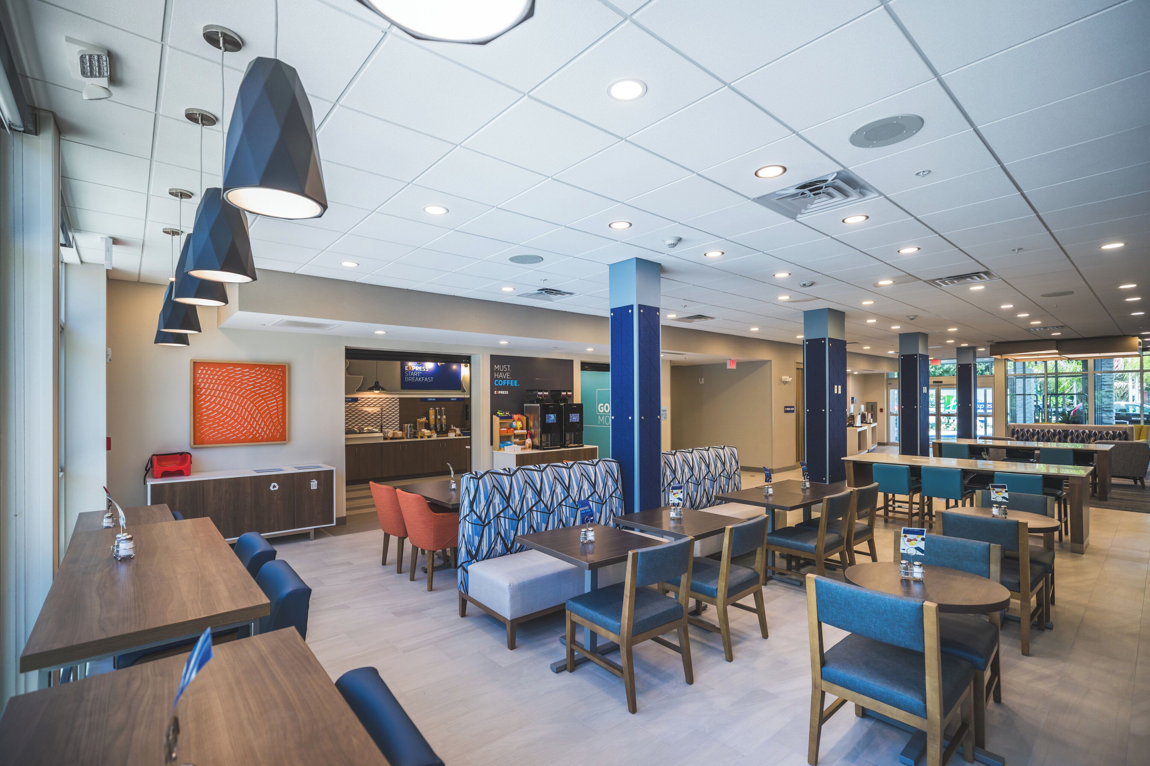 A modern hotel lobby with a coffee bar, seating areas, and a view of the outdoors.