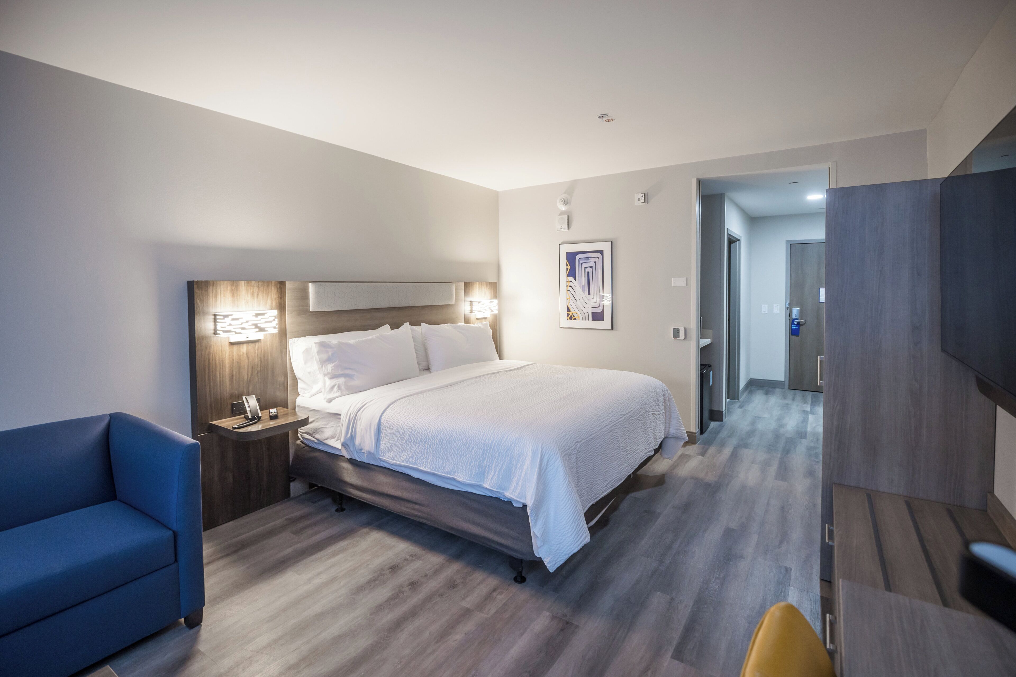 Una habitación de hotel con cama, mesita de noche, lámpara y una silla azul.