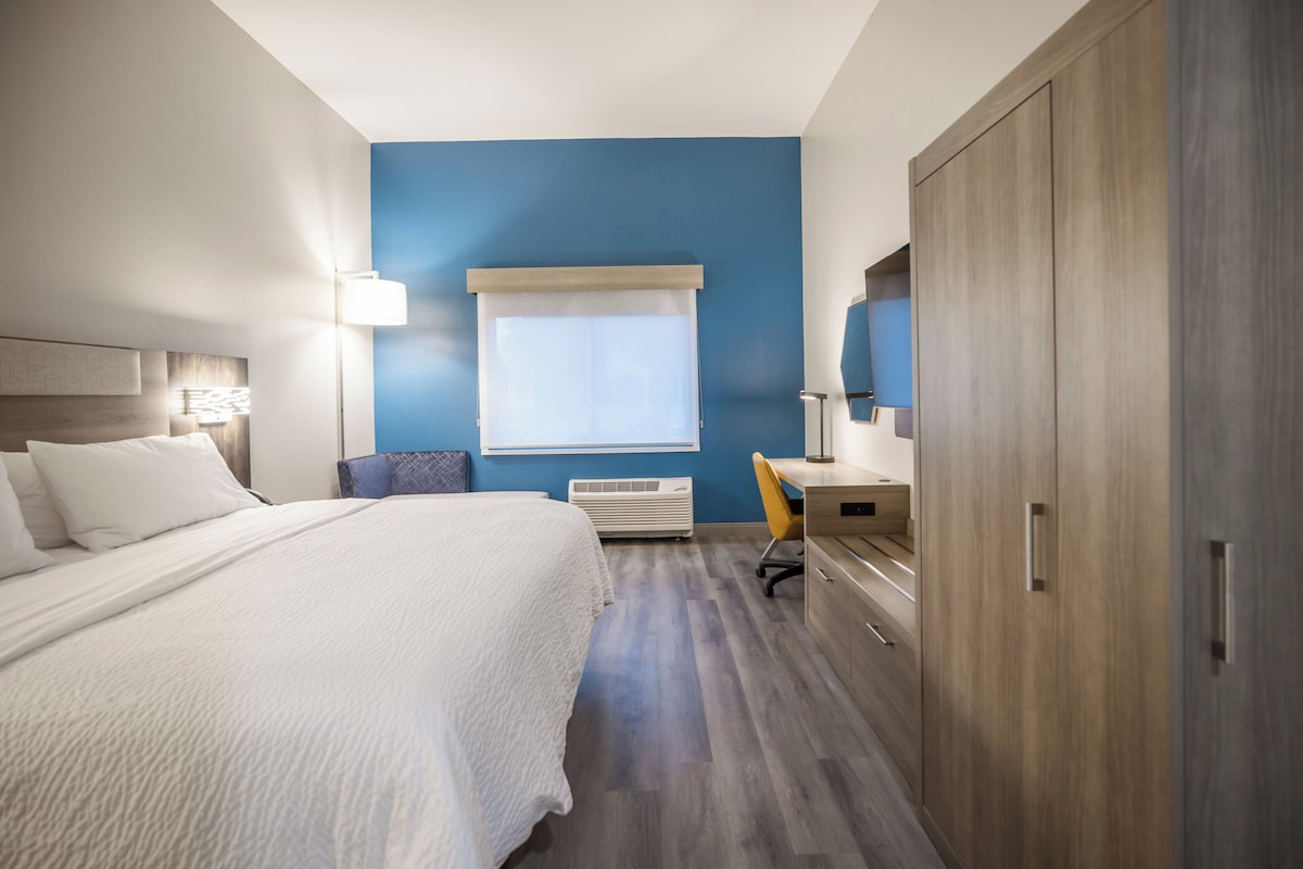 A hotel room with a bed, a desk, a chair, a wardrobe, and a window with blinds.