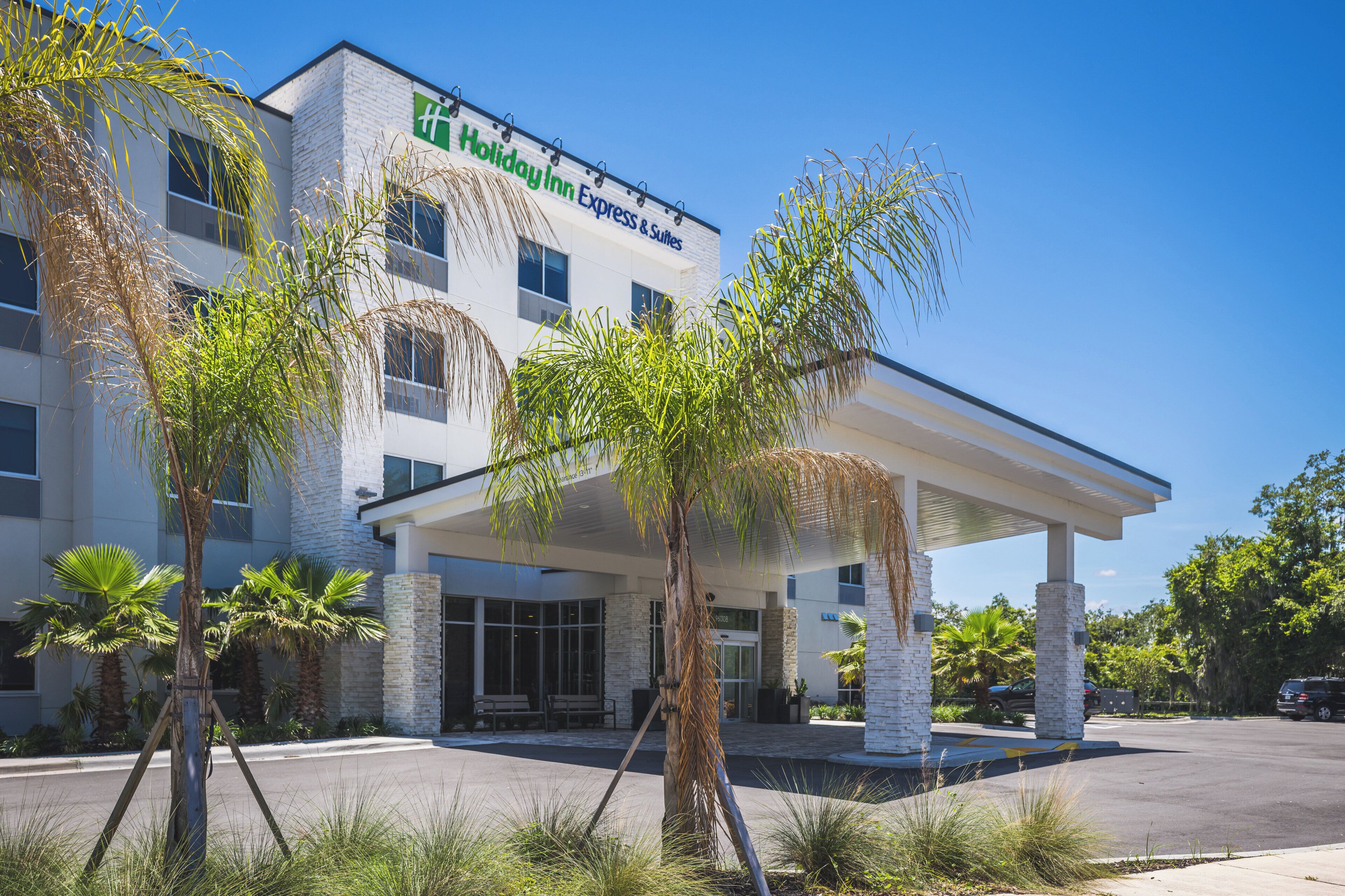 Edificio de Holiday Inn Express & Suites con entrada cubierta, palmeras y un cielo azul claro.