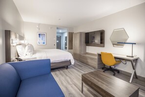 A hotel room with a bed, a desk, a chair, a mirror, and a blue sofa. - Holiday Inn Express & Suites Fernandina Beach Amelia Island by IHG (Fernandina Beach)