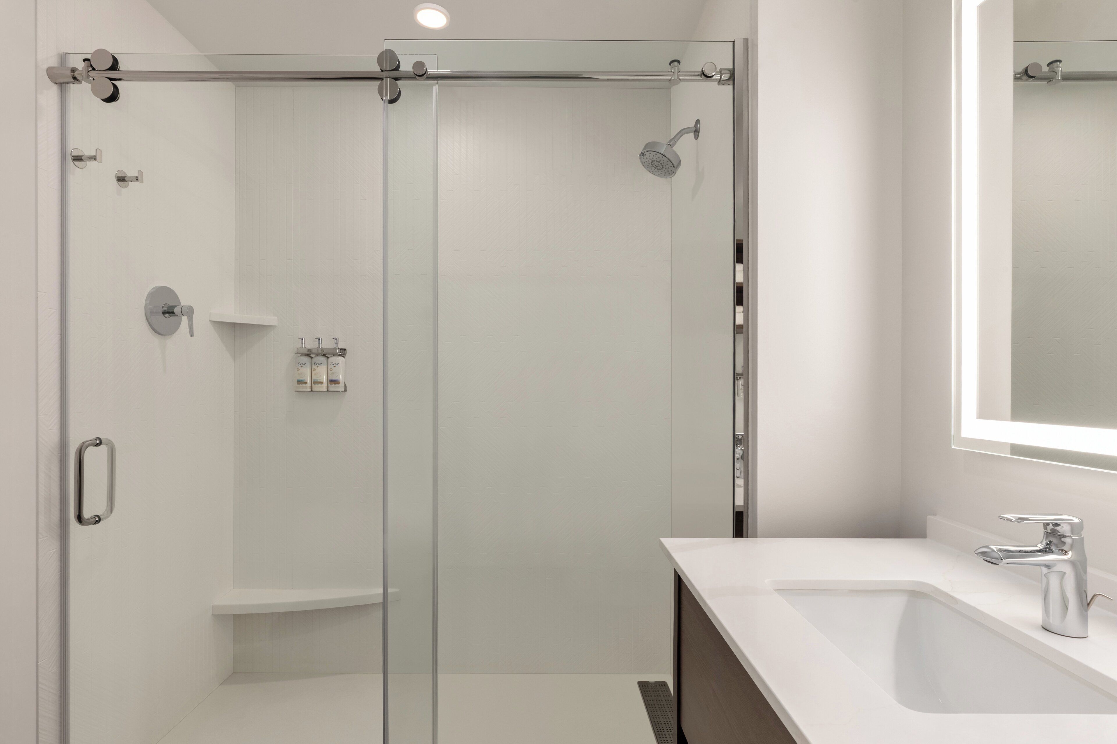 Un bany modern amb una dutxa de vidre, un lavabo blanc i un mirall damunt del lavabo.