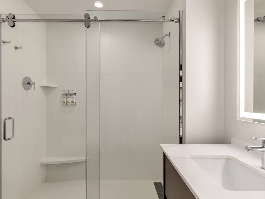 Un bany modern amb una dutxa de vidre, un lavabo blanc i un mirall damunt del lavabo.