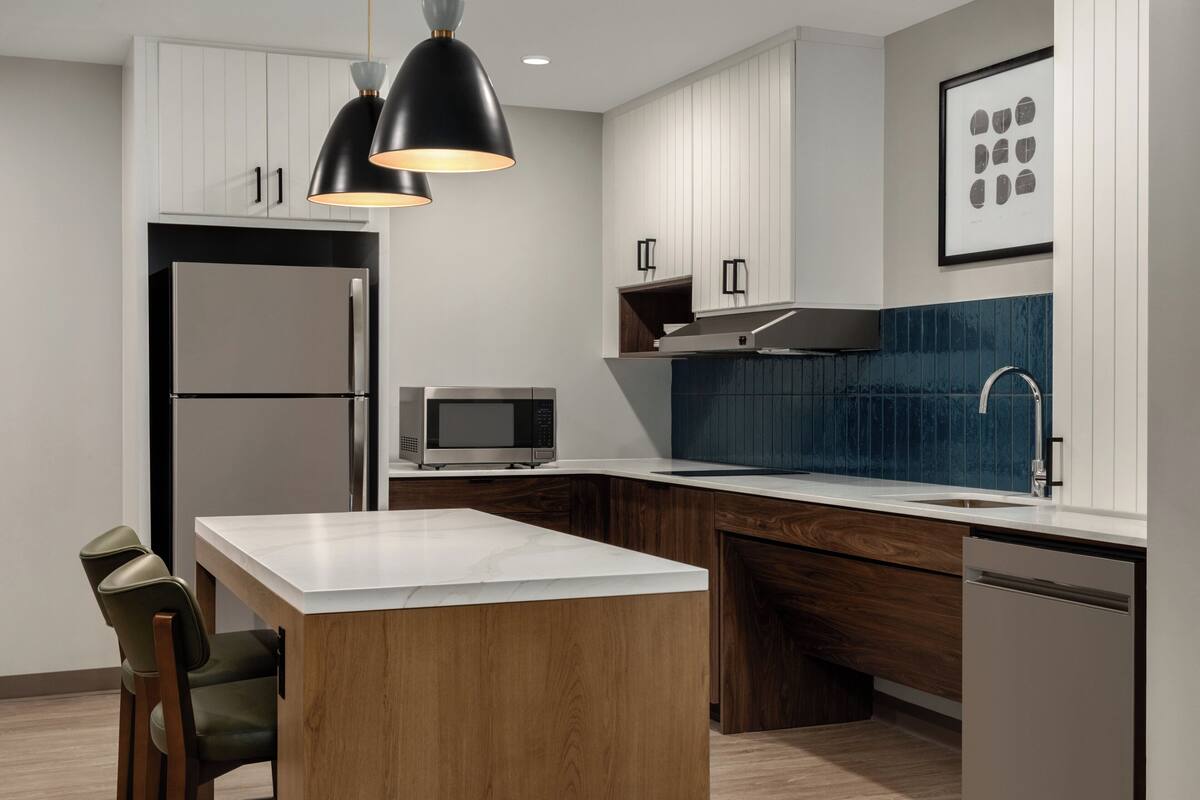 Une cuisine moderne dotée d’un îlot central, d’appareils électroménagers en acier inoxydable et d’un revêtement mural bleu.