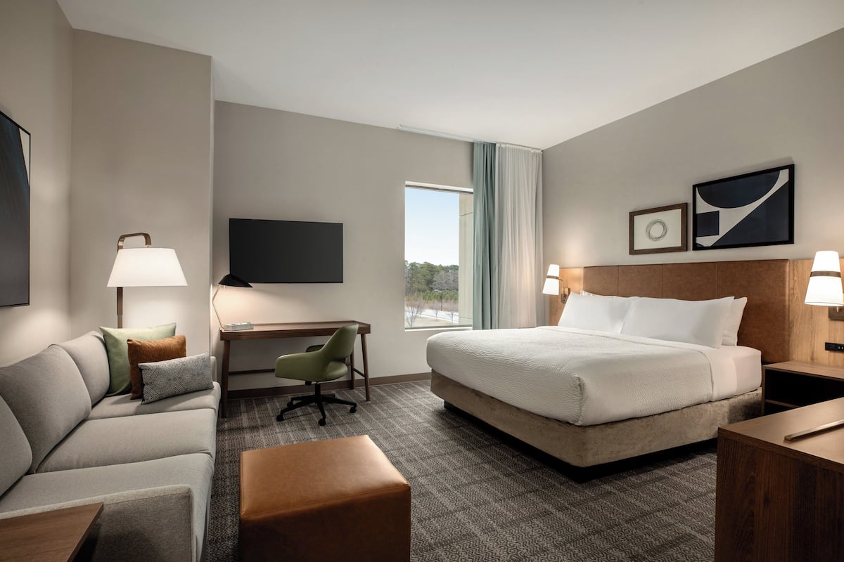 Une chambre d’hôtel équipée d’un lit, d’un bureau, d’une chaise, d’une télévision et d’une fenêtre avec des rideaux.