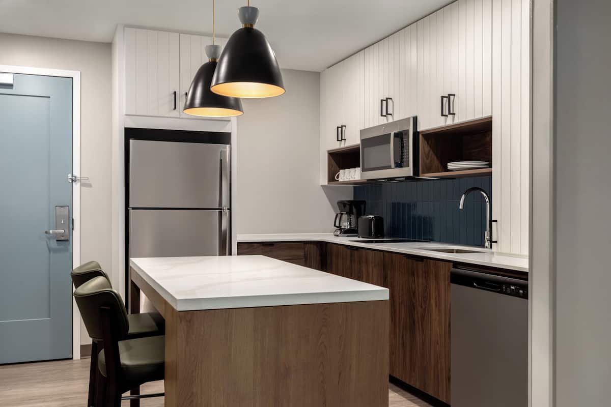 Une cuisine moderne dotée d’un îlot central, d’appareils électroménagers en acier inoxydable et de luminaires suspendus.