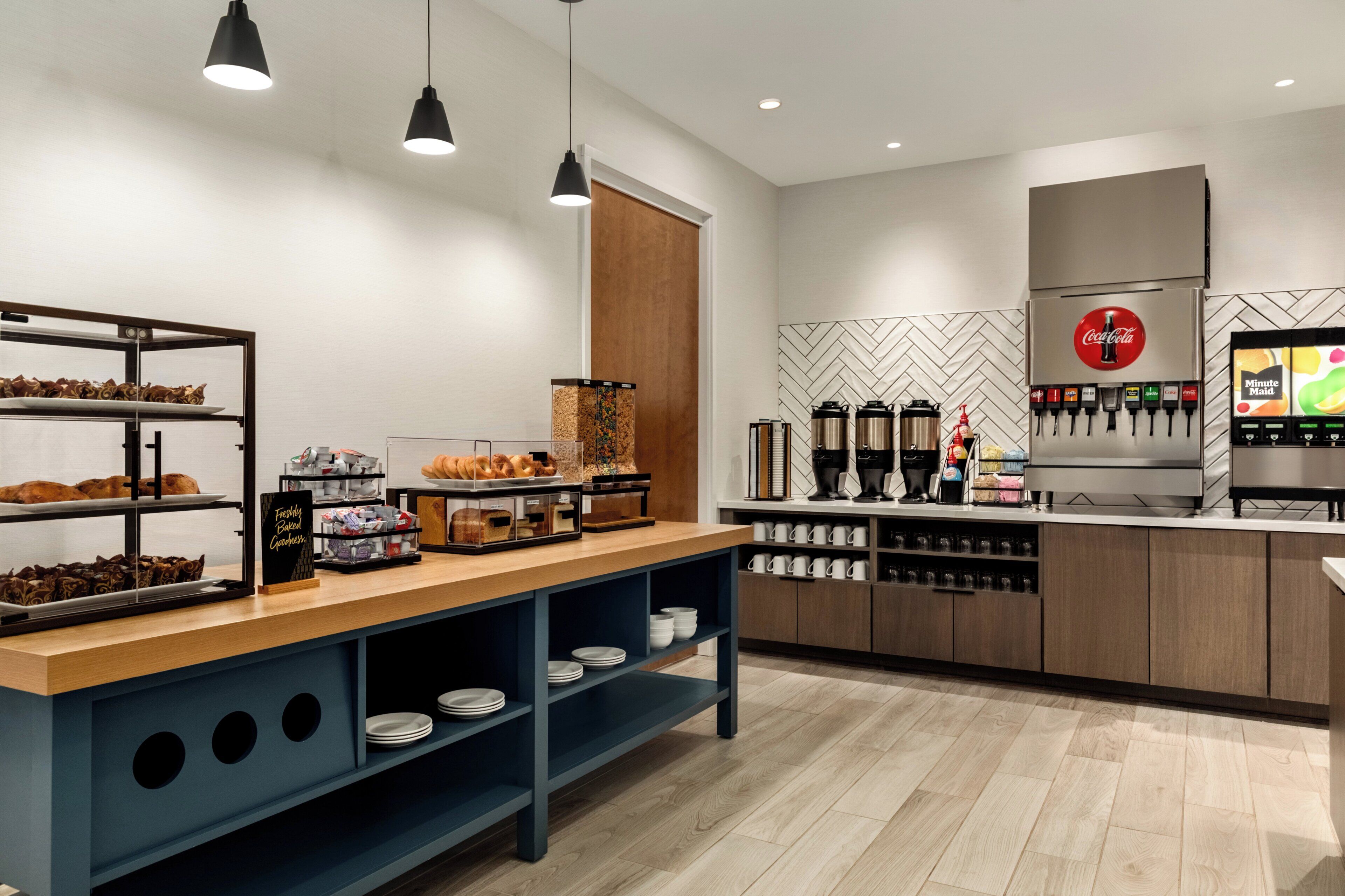 Un área de cocina moderna con una estación de café, un refrigerador y un dispensador de bebidas.
