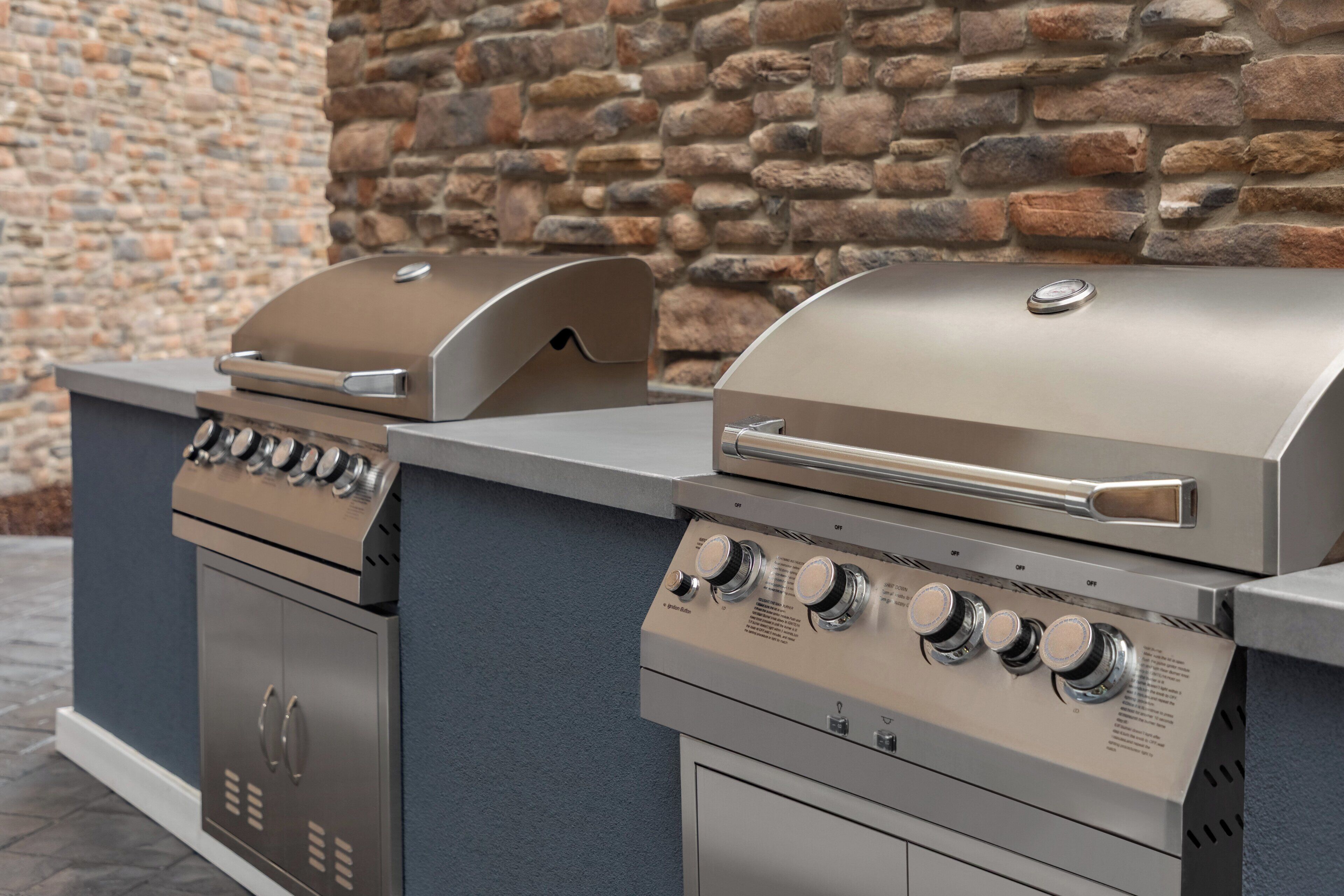 A two-bay outdoor grill station with a stone wall backdrop.