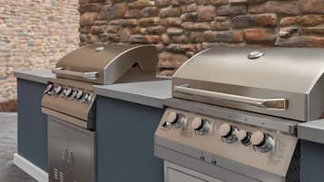 A two-bay outdoor grill station with a stone wall backdrop.