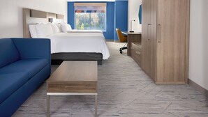 Habitación de hotel moderna con una cama grande, un sofá azul, un escritorio de madera y un armario.