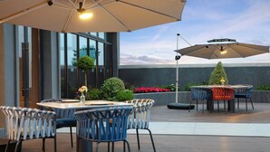 Un patio al aire libre con una mesa redonda y sillas, sombrillas grandes y vistas de un edificio.