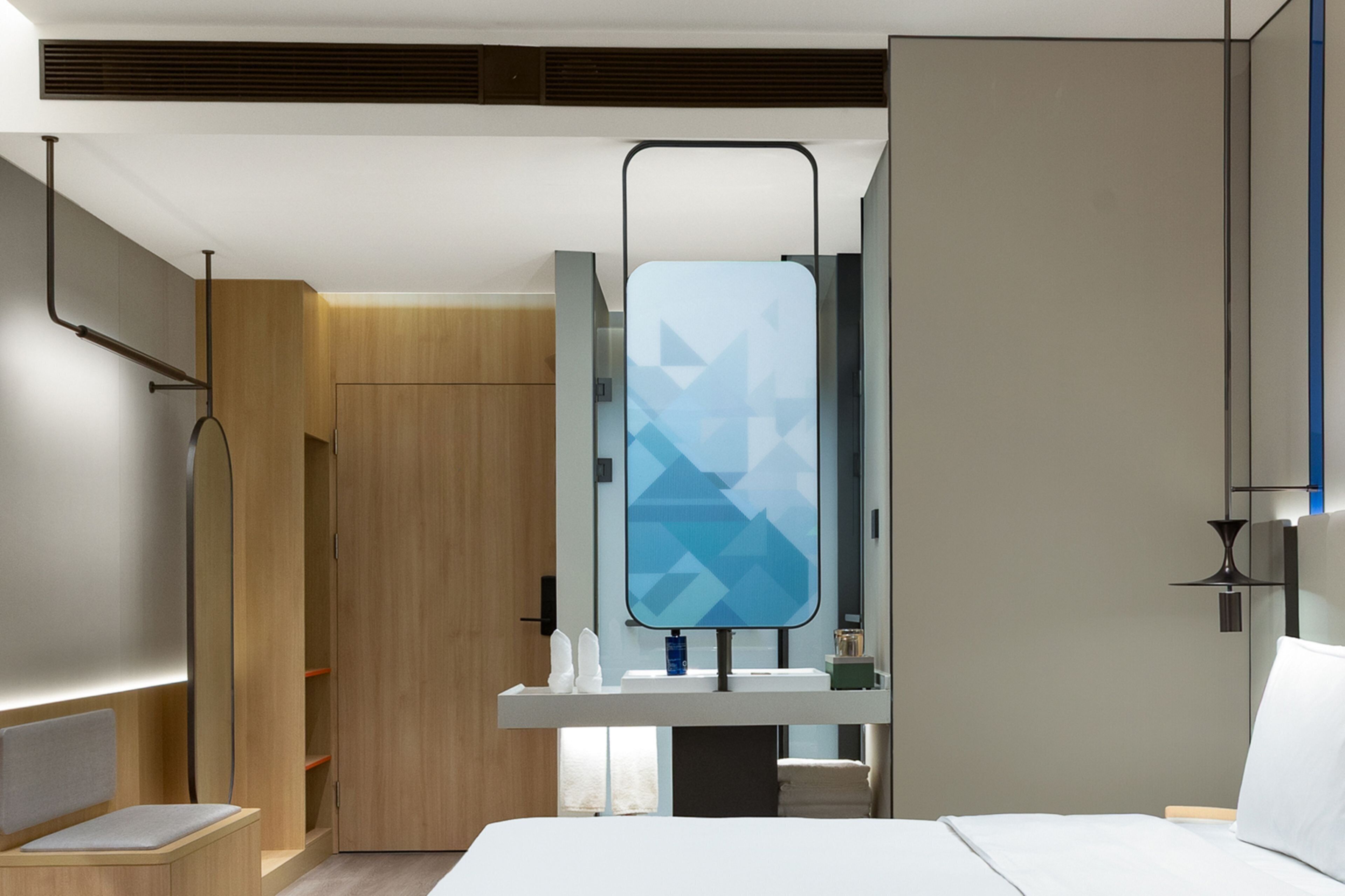 Una habitación de hotel moderna con cama, tocador con espejo, armario de madera y estante empotrado.