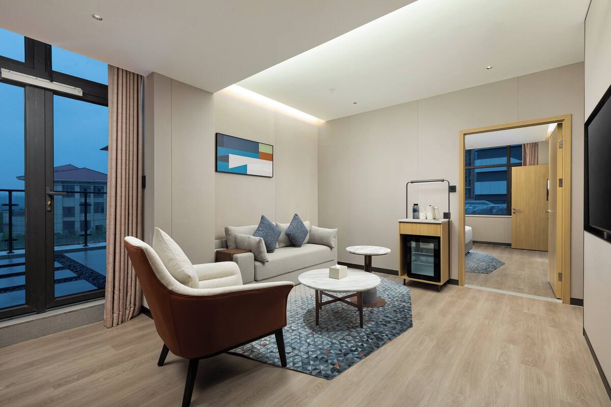 Een moderne hotelkamer met een bank, fauteuil, salontafel en een televisie.