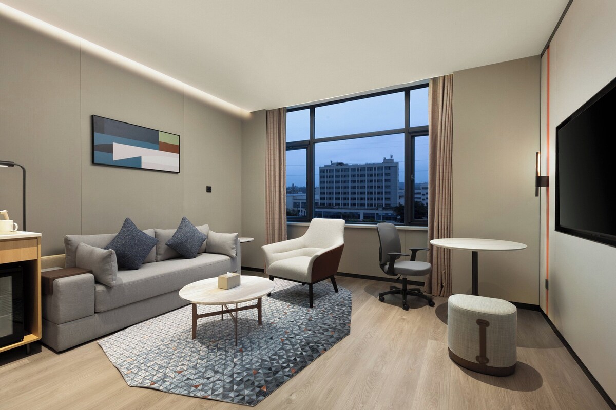 Una habitación de hotel moderna con sofá, sillón, mesa de centro y televisor.